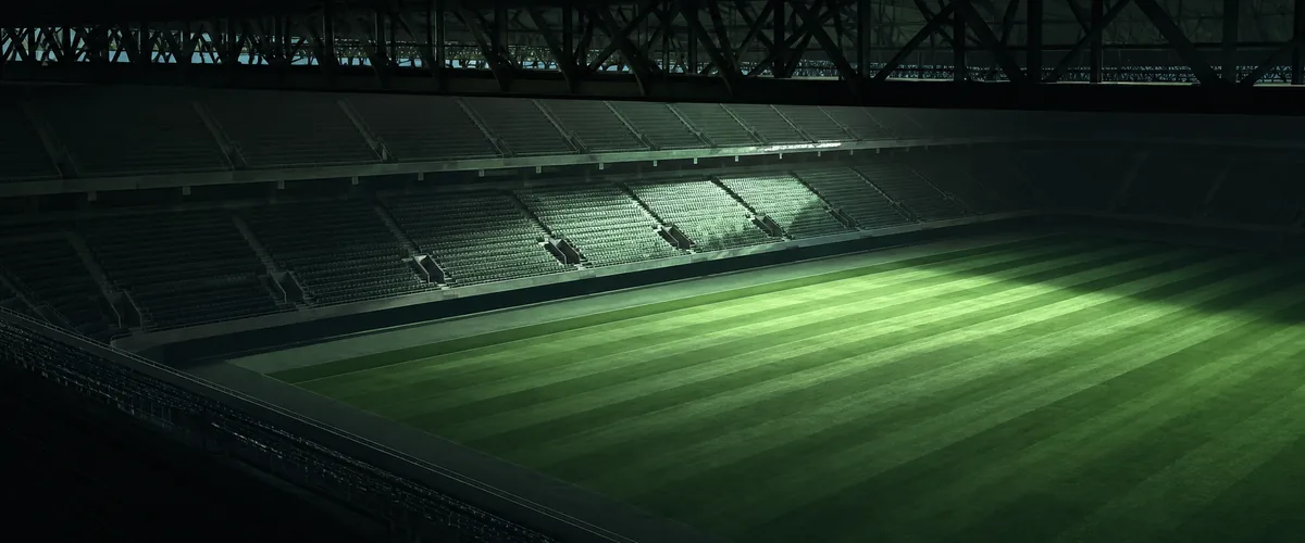 試合のない日の、無人のスタジアム。刈り込みの縞が残る芝の一角に朝の光が落ちている。